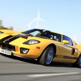 Żółty Ford GT z czarnymi pasami pędzi po torze, w tle widać wiatraki.