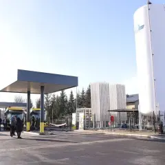 Stacja tankowania CNG. Żółte autobusy czekają pod wiatą, obok wysoki zbiornik i instalacja.