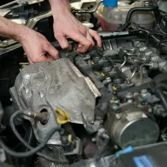 Mechanik pracuje przy silniku, sprawdzając czujnik położenia wałka rozrządu. Objawy awarii mogą być różne, od nierównej pracy po problemy z odpaleniem.
