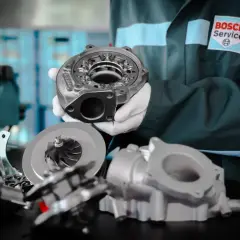 Mechanik w białych rękawiczkach prezentuje części turbosprężarki, w tym wirnik i obudowę. To serce każdego silnika biturbo.