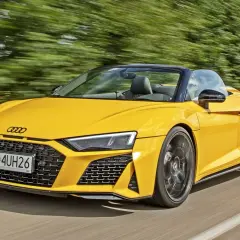 Żółty kabriolet Audi R8 pędzi po drodze, otoczony rozmytym zielonym tłem drzew.