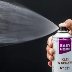Dłoń trzyma puszkę z klejem w sprayu, który jest rozpylany. Idealny klej do podsufitki bez zdejmowania.