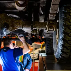 Mechanik sprawdza podwozie terenowego auta z napędem **awd**. Widoczna jest piasta, opona i elementy zawieszenia.