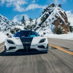 Biały Koenigsegg Agera RS z czarnym pasem pędzi po ośnieżonej górskiej drodze.