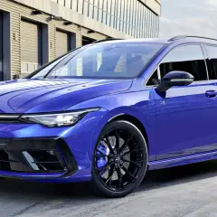 Niebieskie kombi auto Volkswagen Golf R Variant z czarnymi felgami i niebieskimi zaciskami hamulcowymi stoi przed nowoczesnym budynkiem.