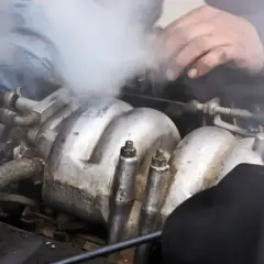 Mechanik próbuje naprawić silnik, z którego wydobywa się biały dym z wydechu.