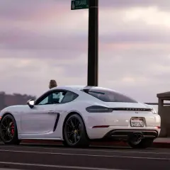 Białe Porsche GT4 z czerwonymi zaciskami hamulcowymi stoi przy drodze z widokiem na ocean.