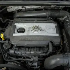 Silnik 2.0 TSI Volkswagena, widok z góry. Widać pokrywę silnika z logo VW i napisem TSI, przewody i inne elementy komory silnika.