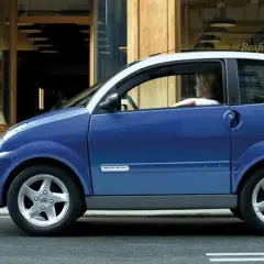 Niebieskie auto od 14 lat, z kobietą za kierownicą, stoi przed sklepem. Obok niego stoi druga kobieta.