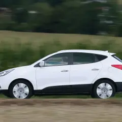 Biały Hyundai ix35 2.0 benzyna w ruchu, z rozmytym tłem zielonych pól i drzew.
