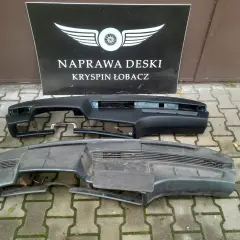 Dwa kokpity samochodowe, jeden czarny, drugi szary, leżą na chodniku przed tablicą z napisem "NAPRAWA DESKI".
