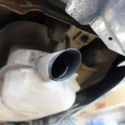 Widok z dołu na rurę wydechową samochodu, sugerującą zapchany dpf objawy. Rdza i sadza wokół rury.