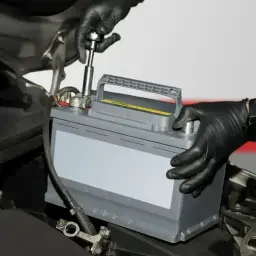 Mechanik w czarnych rękawiczkach dokręca śrubę akumulatora. Proces regeneracji akumulatora w samochodzie.