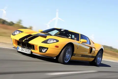 Żółty Ford GT z czarnymi pasami pędzi po torze, w tle widać wiatraki.