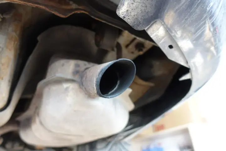Widok z dołu na rurę wydechową samochodu, sugerującą zapchany dpf objawy. Rdza i sadza wokół rury.