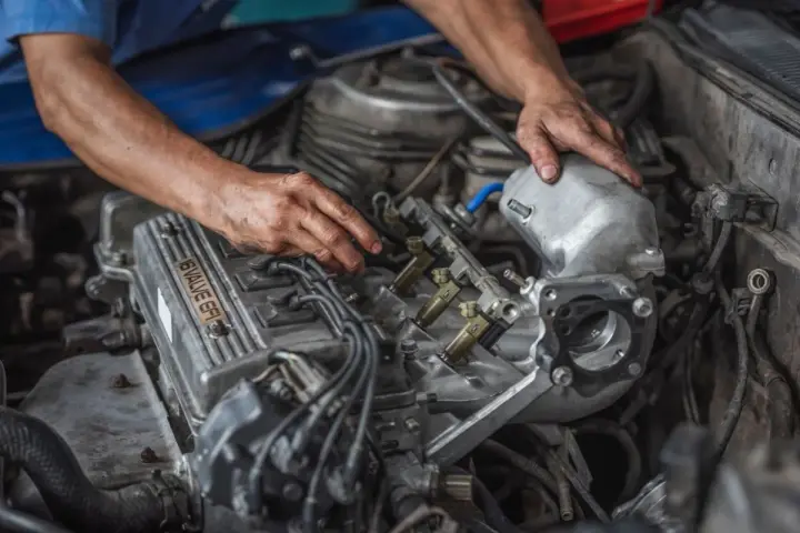 Mechanik pracuje przy silniku. Zbliżenie na dłonie i elementy silnika, w tym wtryskiwacze. Objawy zatarty silnik mogą być różne, ale ten widok sugeruje naprawę.