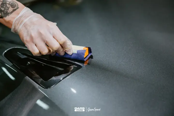 Nakładanie powłoki ceramicznej na auto. Ręka w rękawiczce aplikuje produkt na lakier, nadając mu połysk i ochronę.