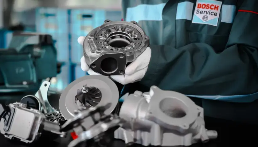 Mechanik w białych rękawiczkach prezentuje części turbosprężarki, w tym wirnik i obudowę. To serce każdego silnika biturbo.