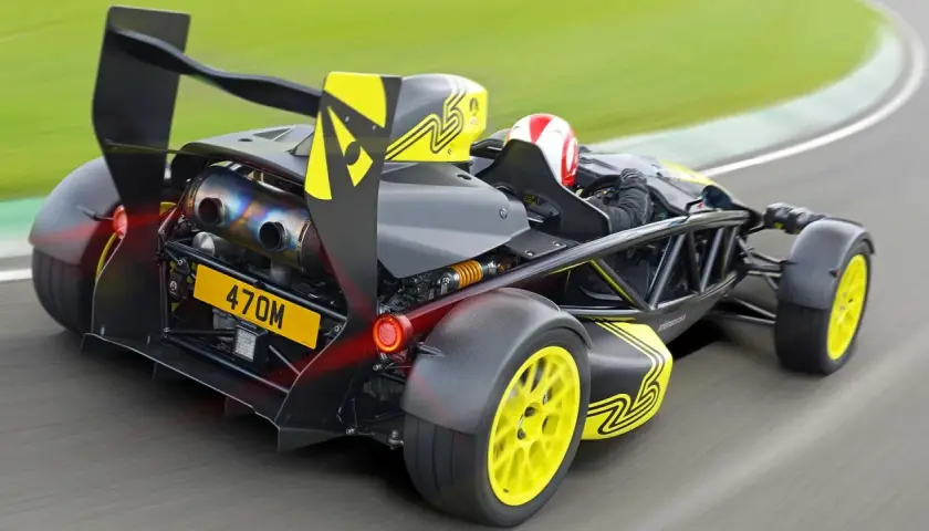 Ariel Atom na torze wyścigowym, z kierowcą w kasku, żółtymi felgami i czarnym spojlerem.