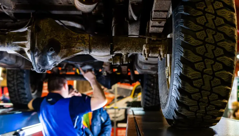 Mechanik sprawdza podwozie terenowego auta z napędem **awd**. Widoczna jest piasta, opona i elementy zawieszenia.