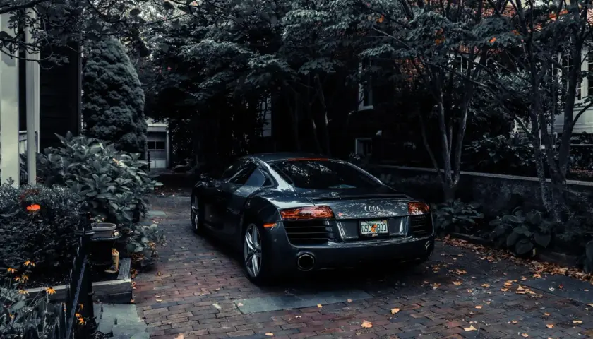 Ciemnoszary samochód sportowy Audi R8 zaparkowany na ceglanej podjazdów wśród drzew.