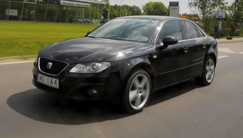 Czarny Seat Exeo 2.0 TDI w ruchu, z widocznym salonem Audi w tle.