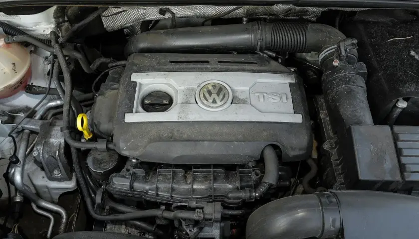 Silnik 2.0 TSI Volkswagena, widok z góry. Widać pokrywę silnika z logo VW i napisem TSI, przewody i inne elementy komory silnika.
