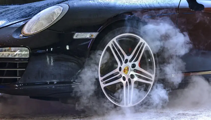 Czarny Porsche z dymem unoszącym się z koła. Sprawdź ozonowanie samochodu cennik, by odświeżyć wnętrze.
