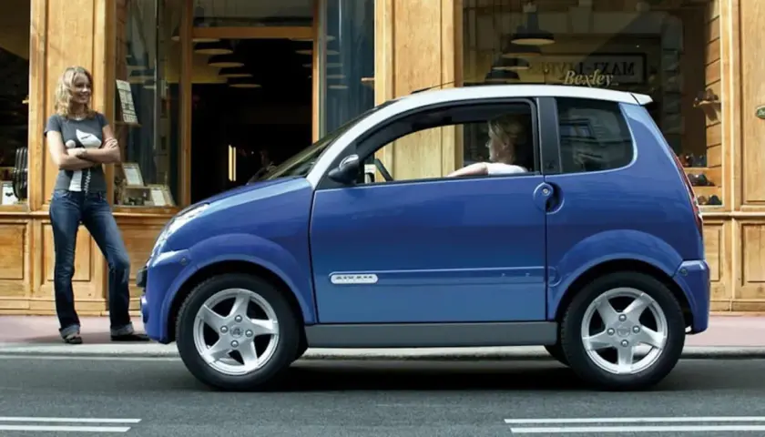 Niebieskie auto od 14 lat, z kobietą za kierownicą, stoi przed sklepem. Obok niego stoi druga kobieta.