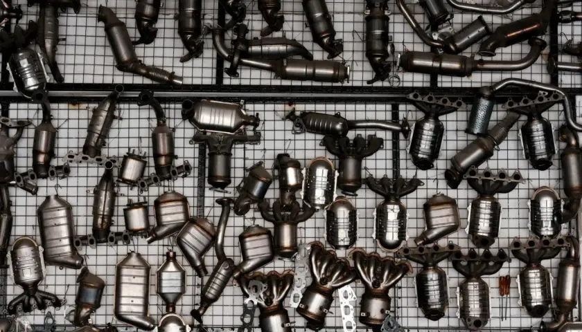 Duża kolekcja metalowych części samochodowych, głównie katalizatorów, wiszących na siatce.