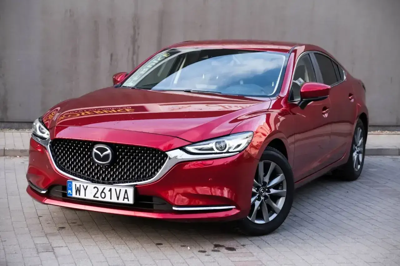 Czerwona Mazda 6 2.0 benzyna z polskimi tablicami rejestracyjnymi stoi na chodniku.