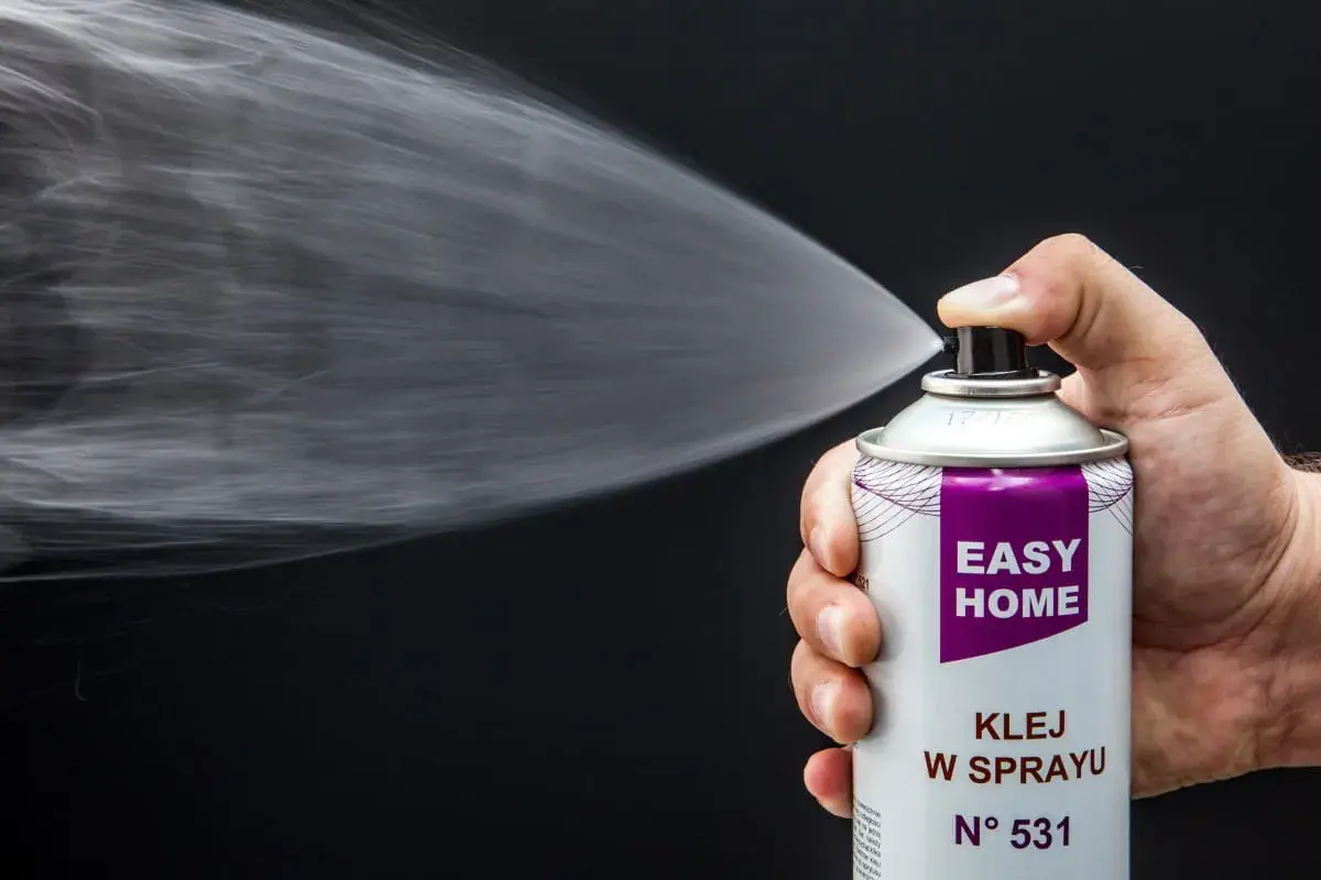 Dłoń trzyma puszkę z klejem w sprayu, który jest rozpylany. Idealny klej do podsufitki bez zdejmowania.