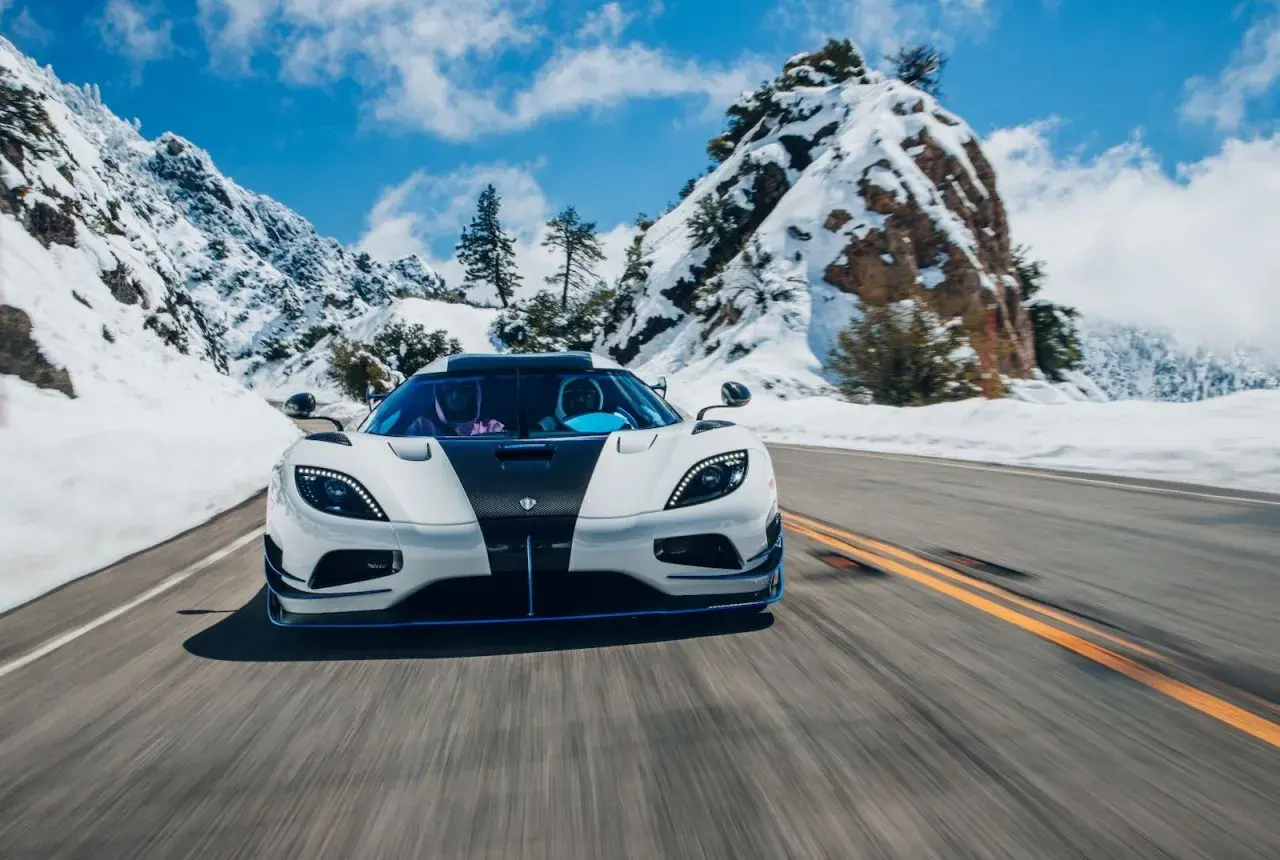 Biały Koenigsegg Agera RS z czarnym pasem pędzi po ośnieżonej górskiej drodze.