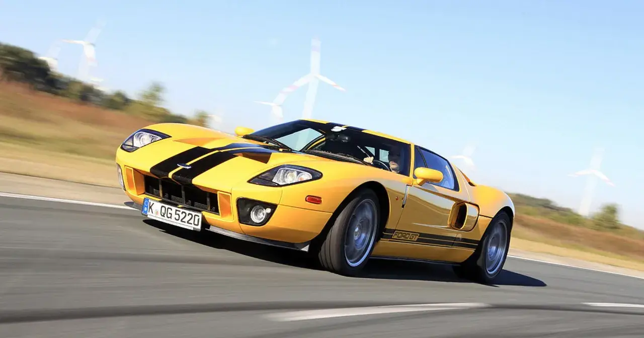 Żółty Ford GT z czarnymi pasami pędzi po torze, w tle widać wiatraki.