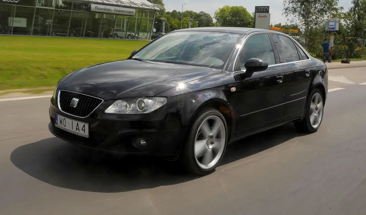 Czarny Seat Exeo 2.0 TDI w ruchu, z widocznym salonem Audi w tle.