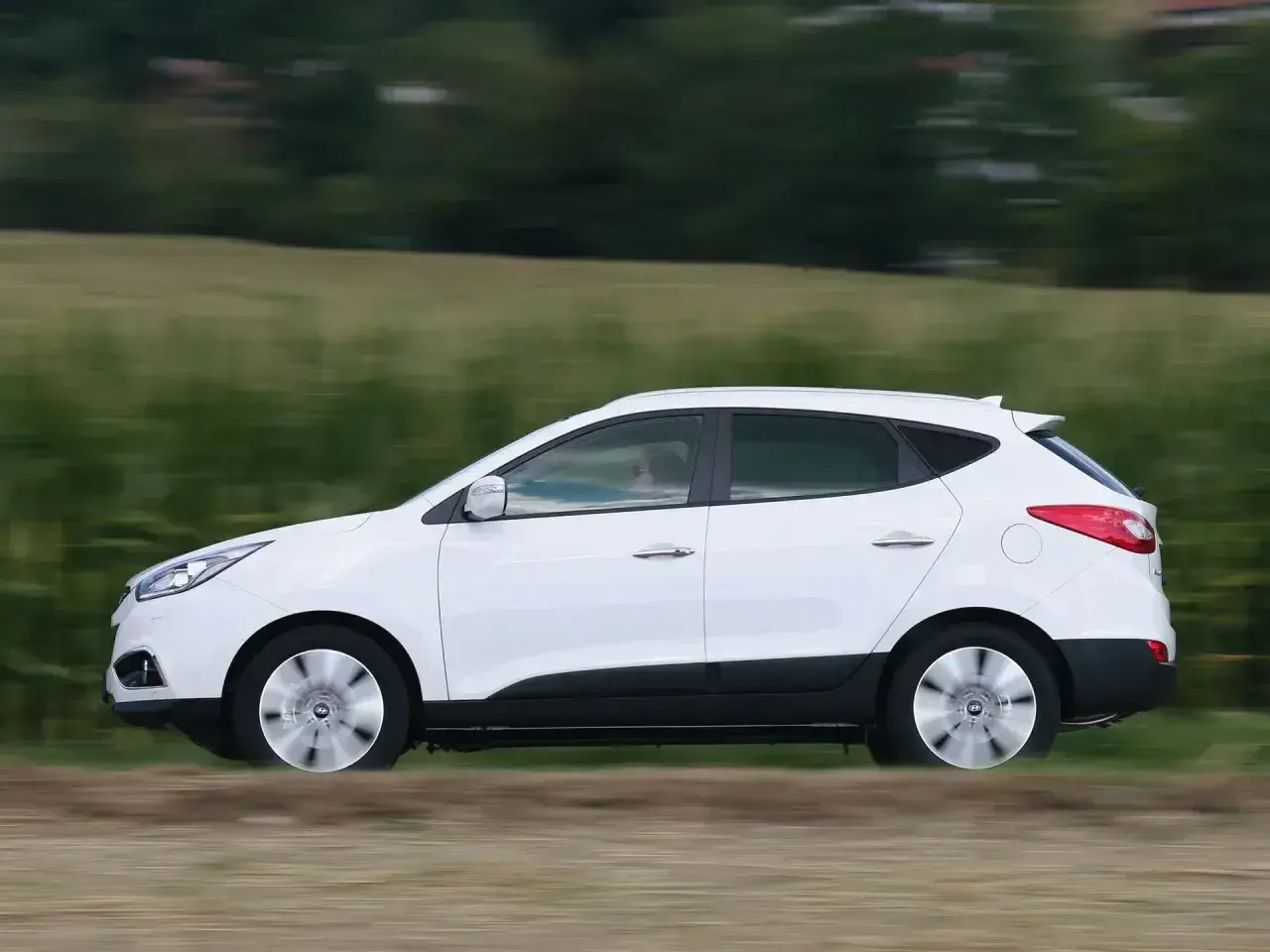 Biały Hyundai ix35 2.0 benzyna w ruchu, z rozmytym tłem zielonych pól i drzew.
