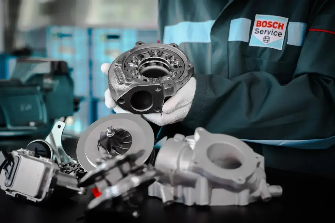Mechanik w rękawiczkach prezentuje turbosprężarkę, kluczowy element zwiększający moc silnika w samochodzie.