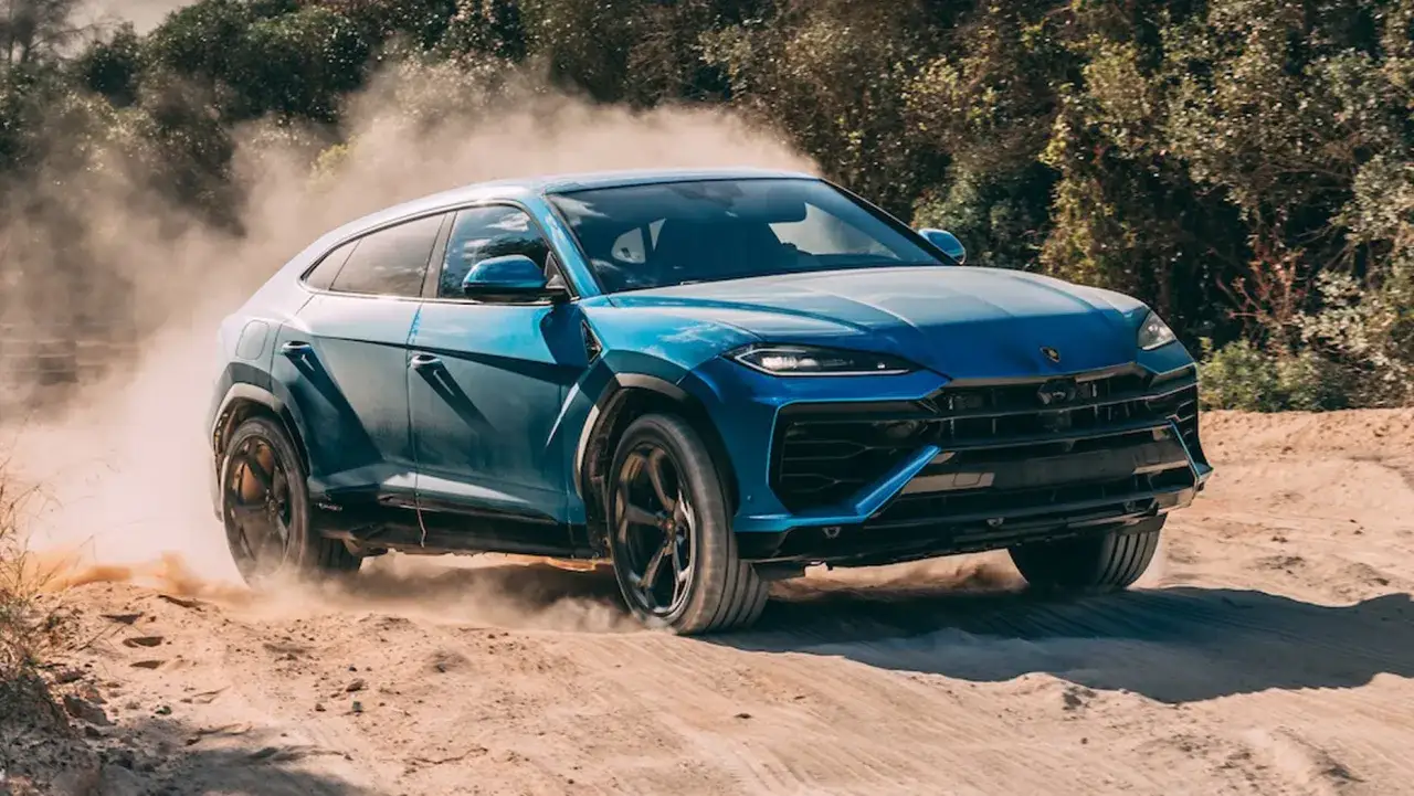Niebieskie, nowe Lamborghini Urus szaleje po piaszczystym terenie, wzbijając tumany kurzu.