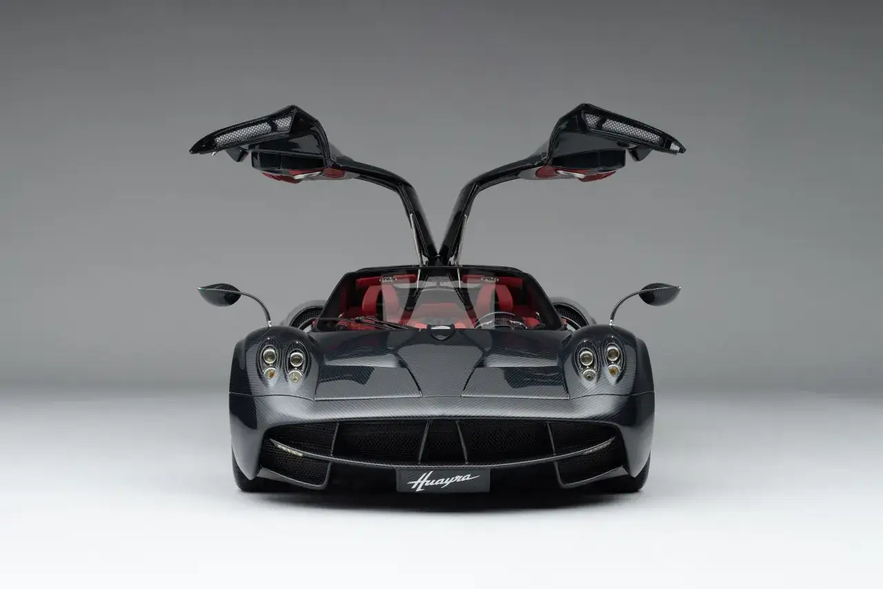 Czarny Pagani Huayra z otwartymi drzwiami typu gullwing i czerwonym wnętrzem, prezentujący swoje karbonowe nadwozie.
